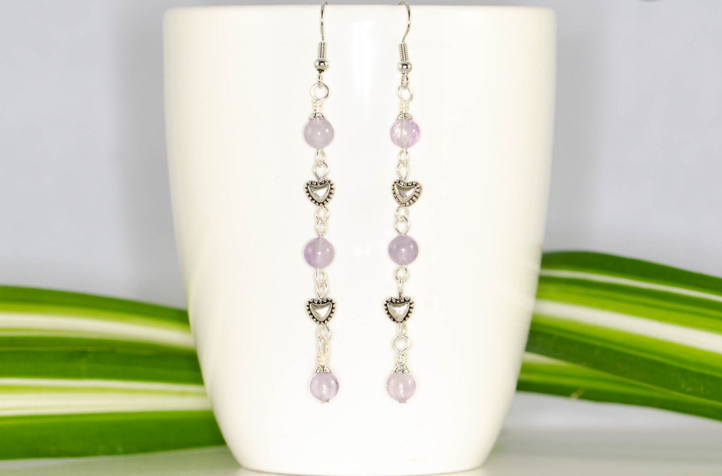 Long Amethyst and Heart Earrings displayed on a coffee mug.