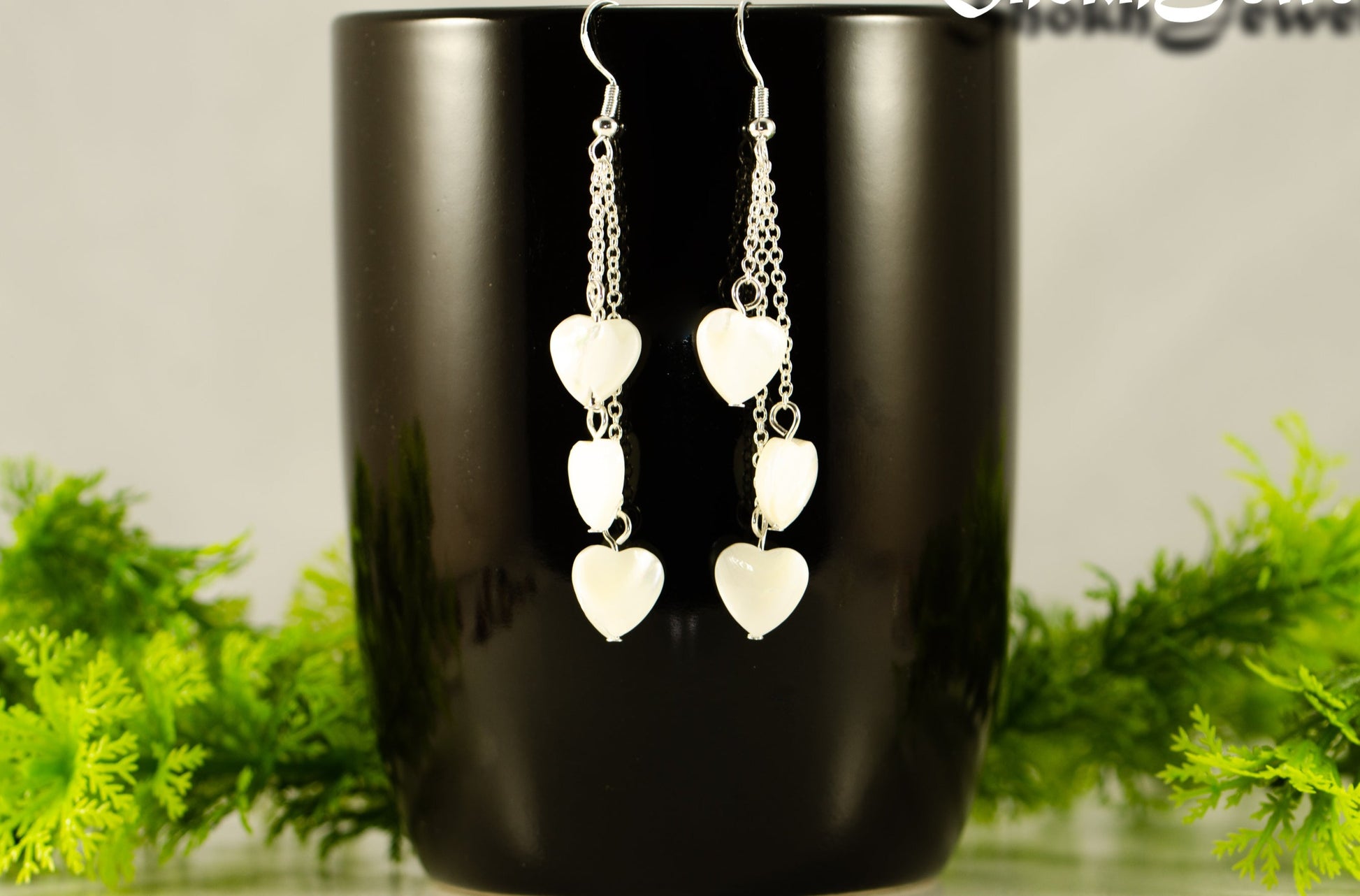 Long Silver Plated Chain and Seashell Heart Earrings displayed on a coffee mug.