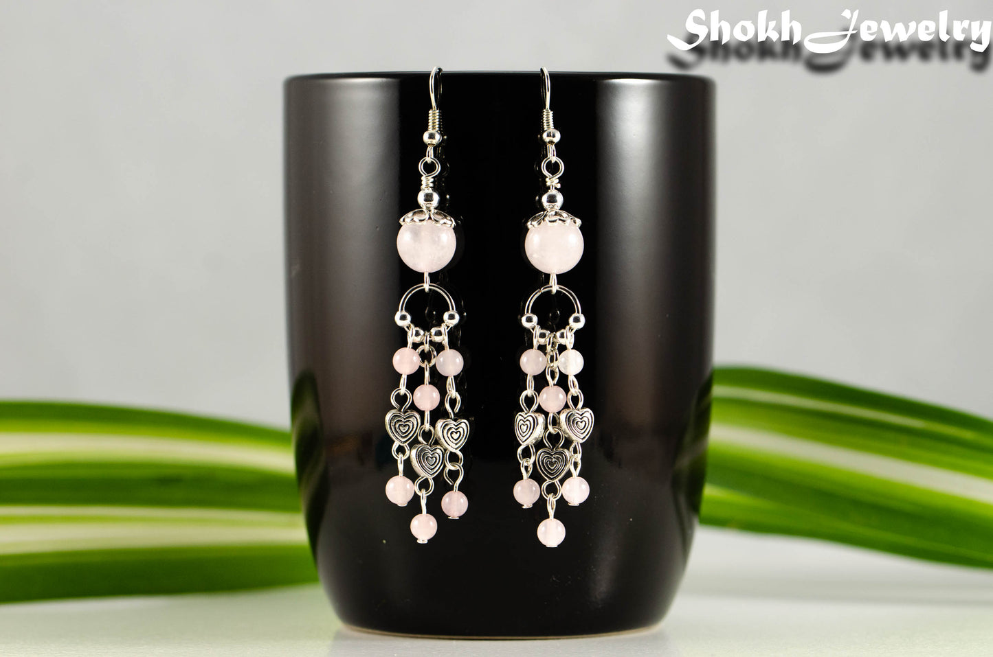 Statement Rose Quartz and Heart Chandelier Earrings displayed on a black coffee mug.