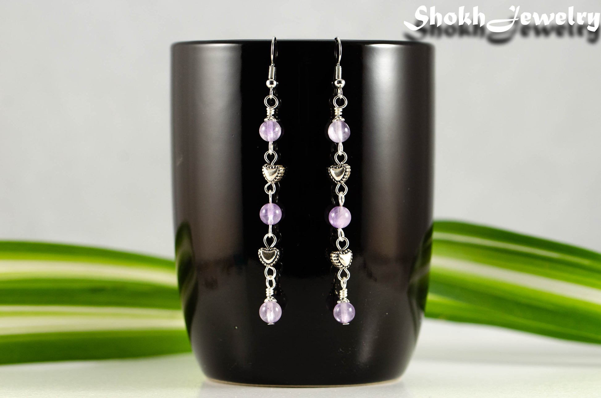 Long Amethyst and Heart Earrings displayed on a coffee mug.