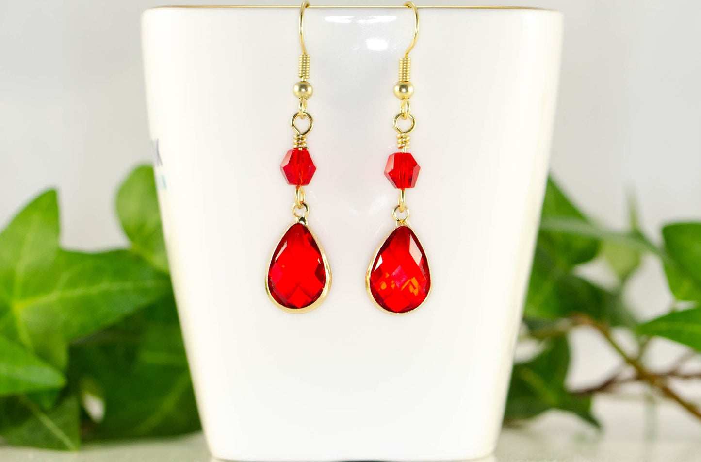 Red Glass Teardrop Dangle Earrings displayed on a tea cup.