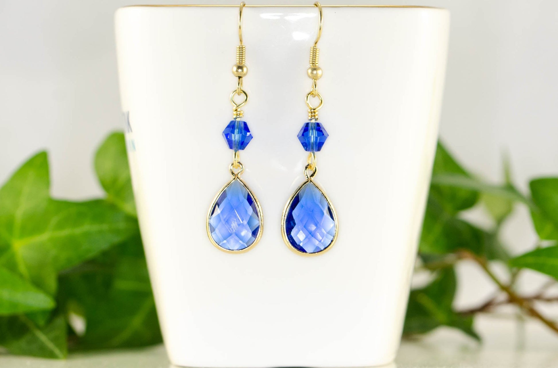 Blue Glass Teardrop Dangle Earrings displayed on a tea cup.