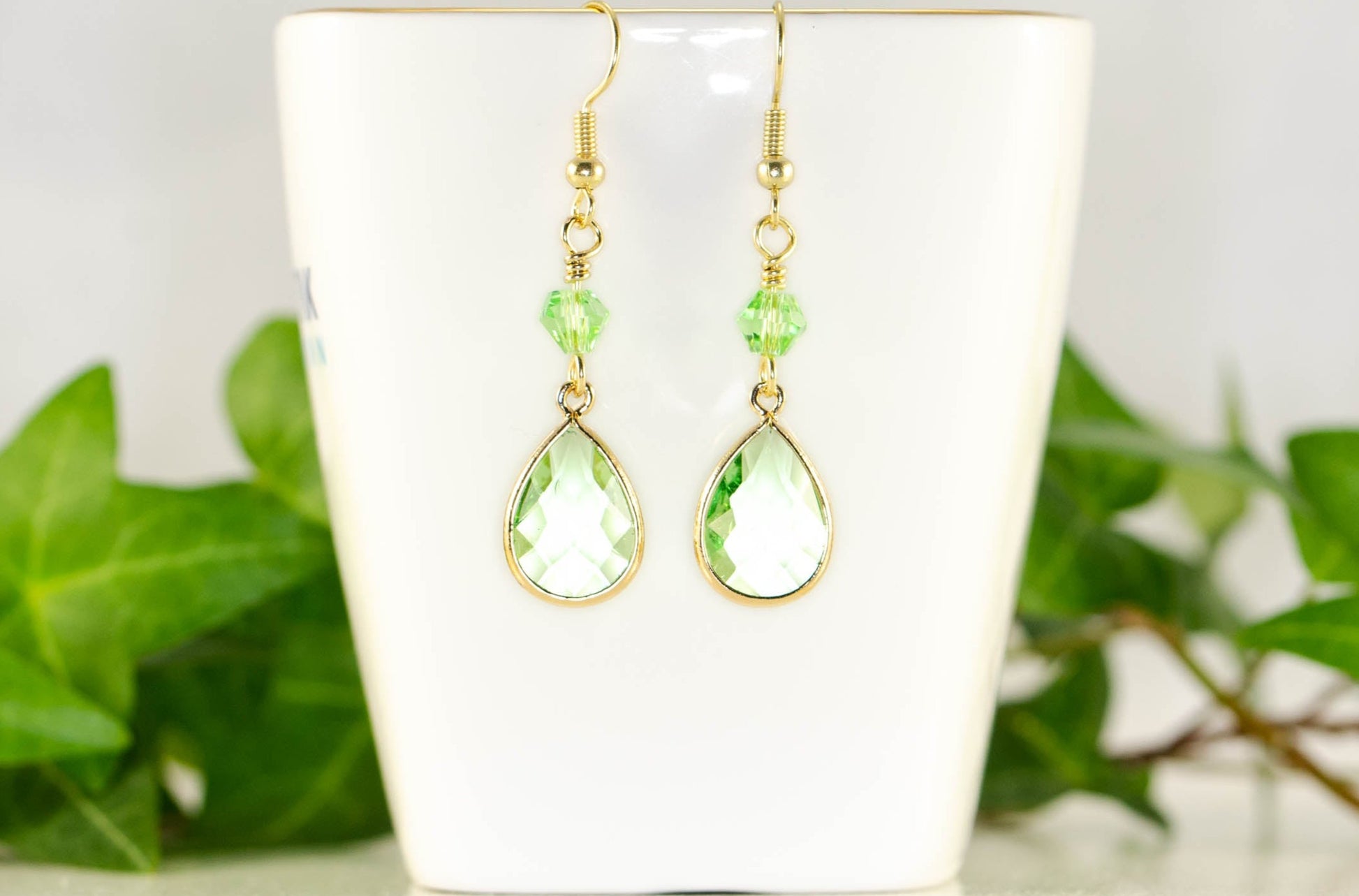 Green Glass Teardrop Dangle Earrings displayed on a tea cup.