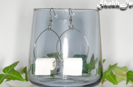 Large Miniature Toilet Paper Roll Earrings displayed on a glass.