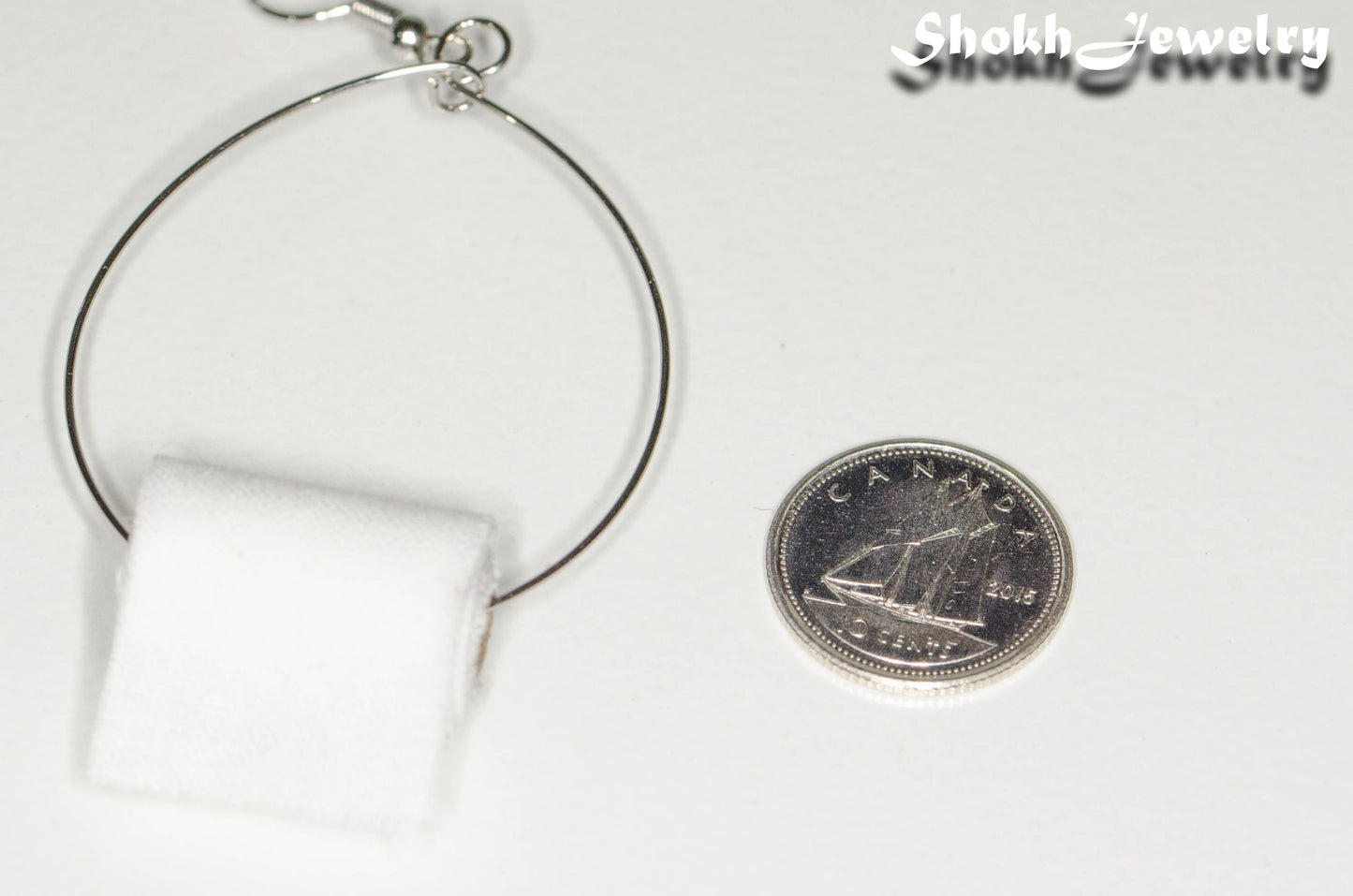 Close up of Large Miniature Toilet Paper Roll Earring beside a dime.