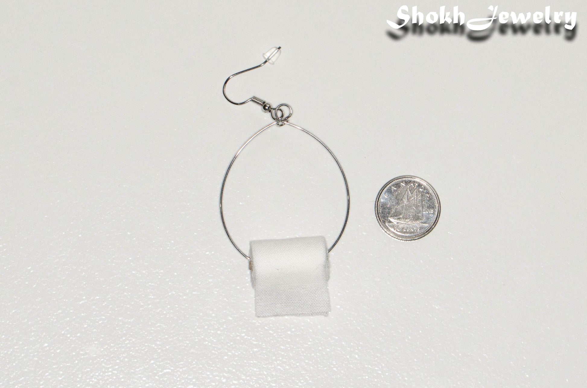 Large Miniature Toilet Paper Roll Earring beside a dime.