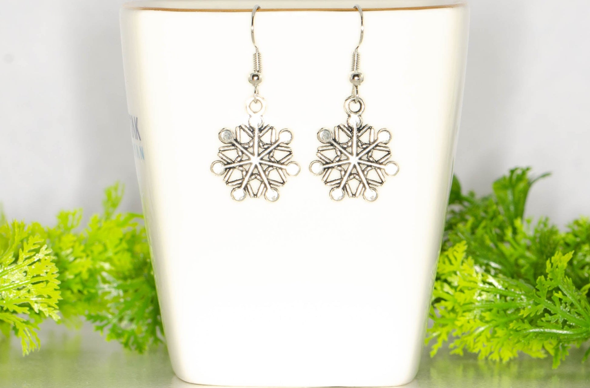 Christmas Snowflakes Charm Earrings displayed on a tea cup.