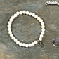 6mm White Howlite Bracelet with Initial beside a dime.