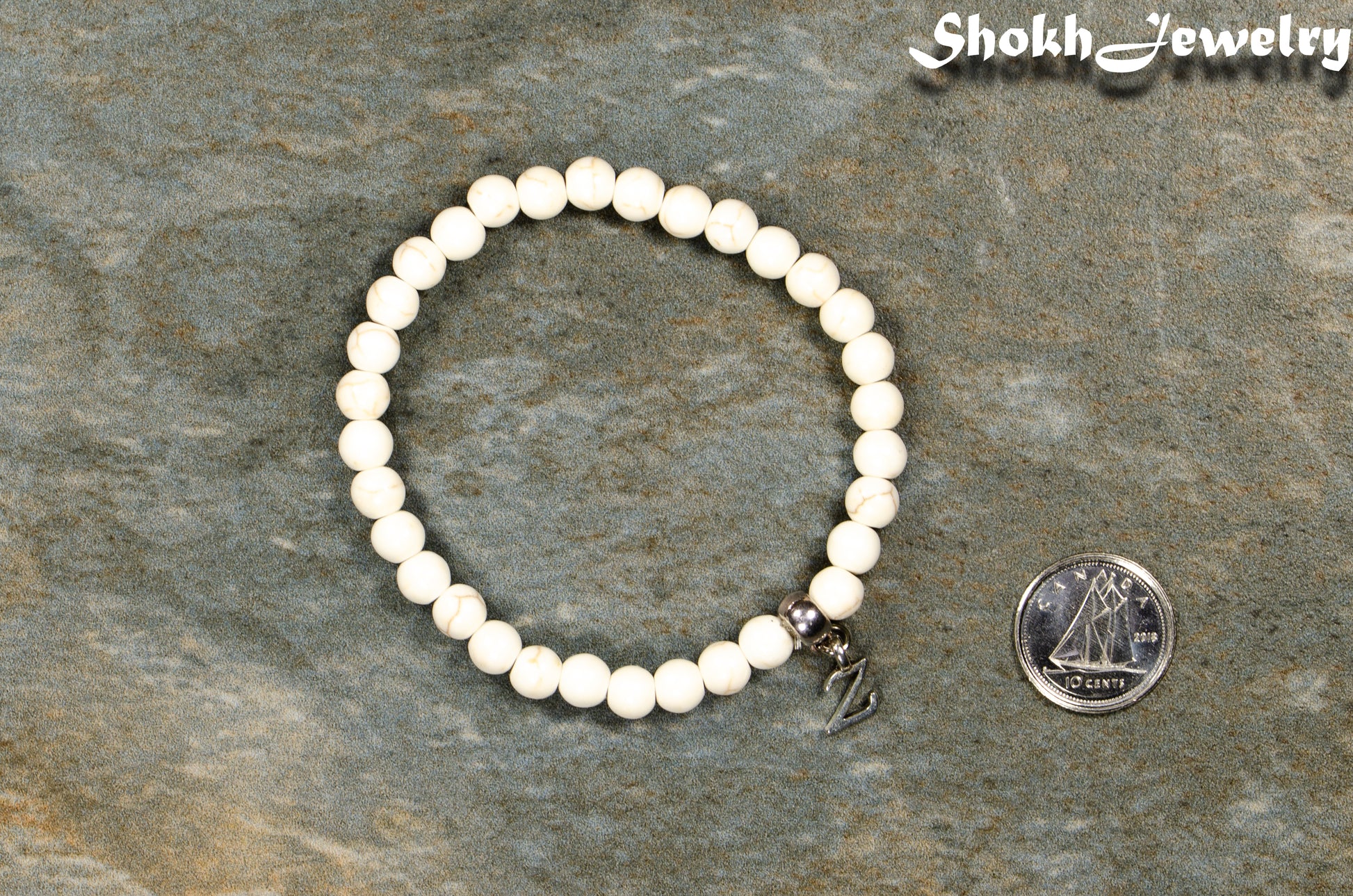 6mm White Howlite Bracelet with Initial beside a dime.