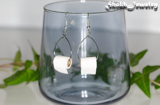 Miniature Toilet Paper Roll Earrings displayed on a glass.
