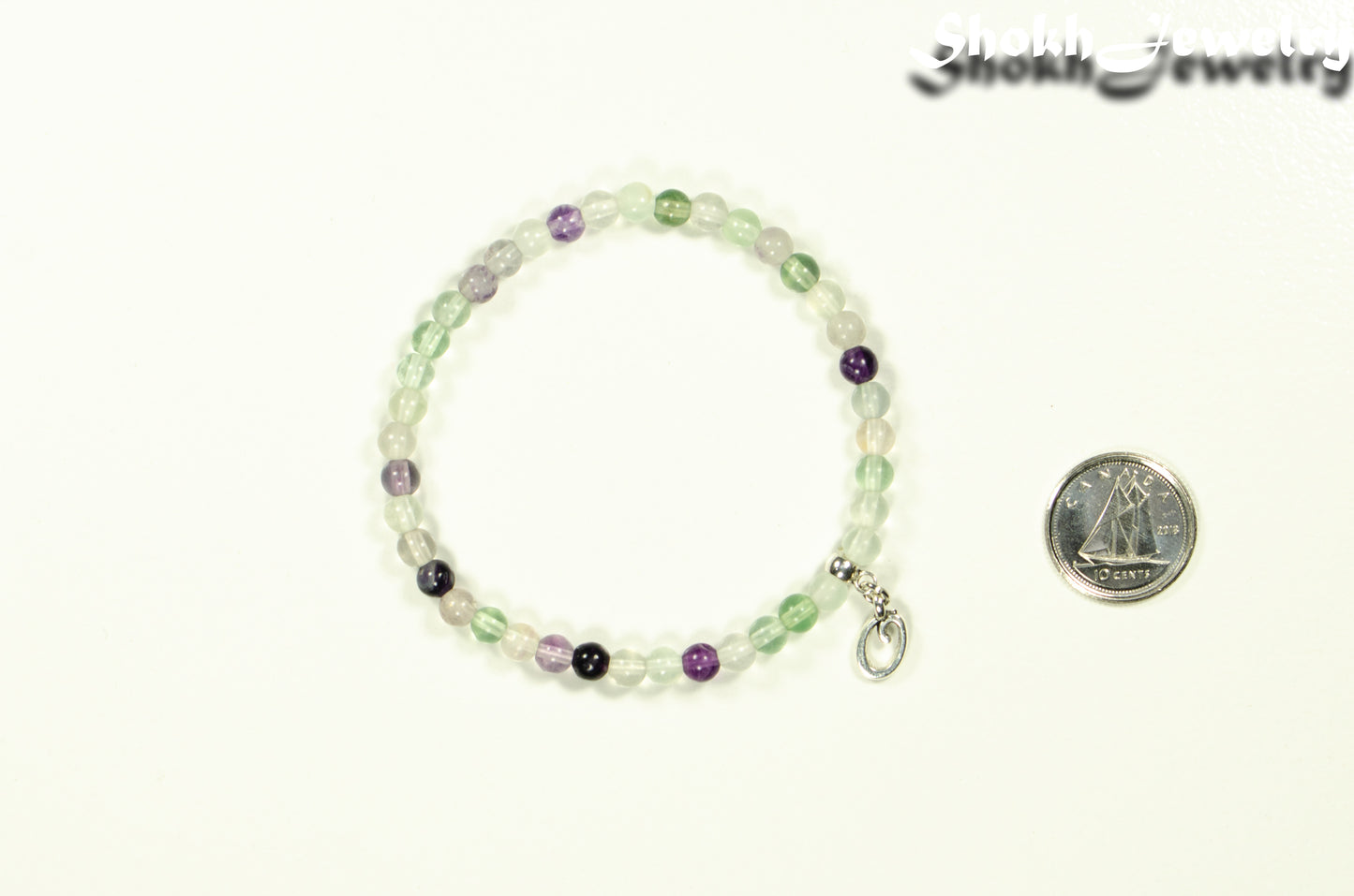 4mm Rainbow Fluorite Bracelet with Initial beside a dime.