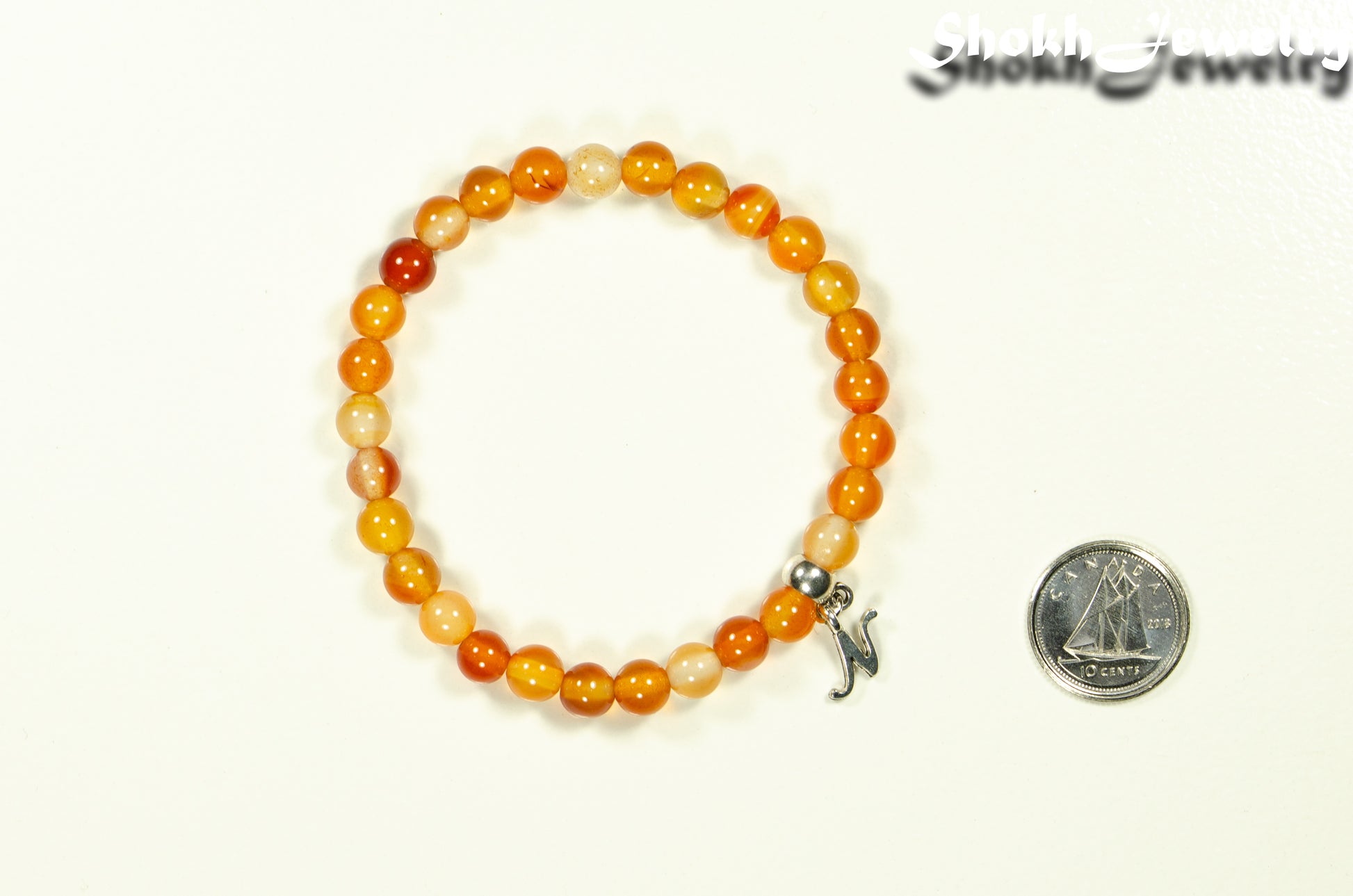 6mm Carnelian Bracelet with Initial beside a dime.