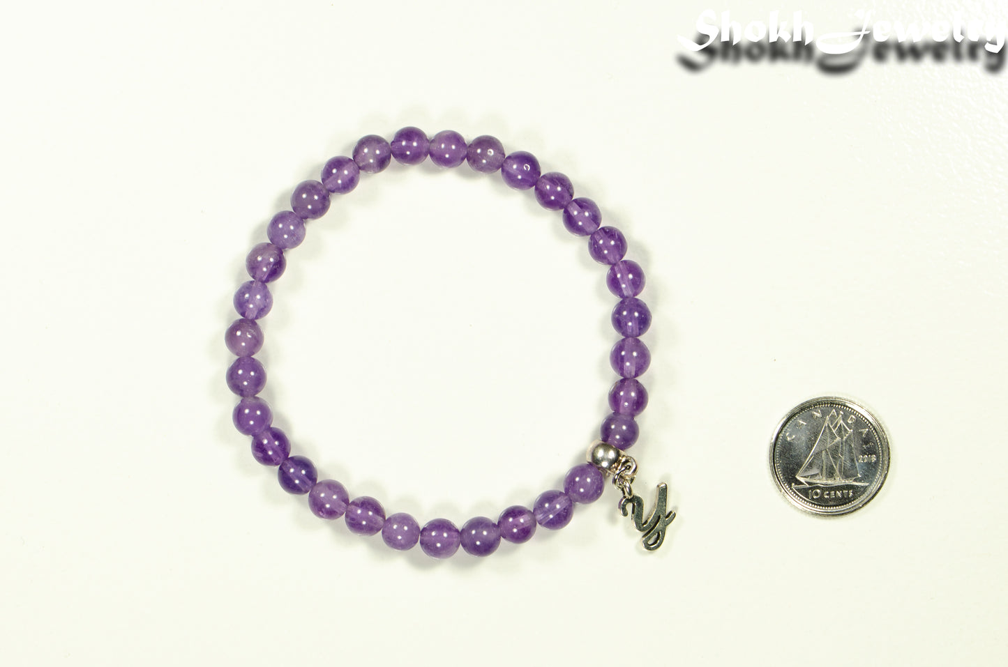 6mm Amethyst Bracelet with Initial beside a dime.