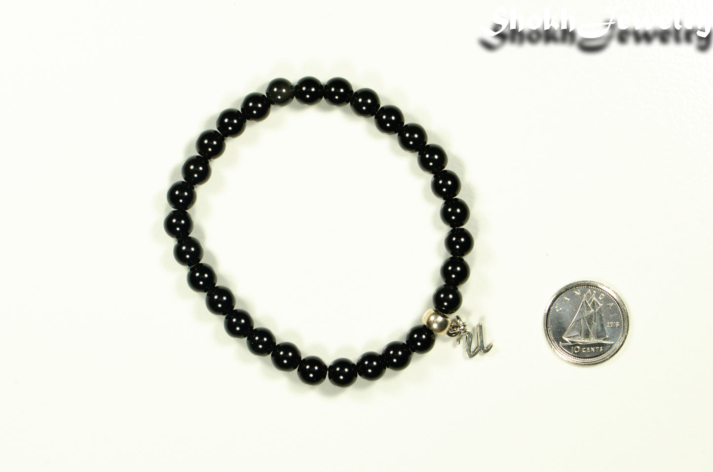 6mm Black Obsidian Bracelet with Initial beside a dime.