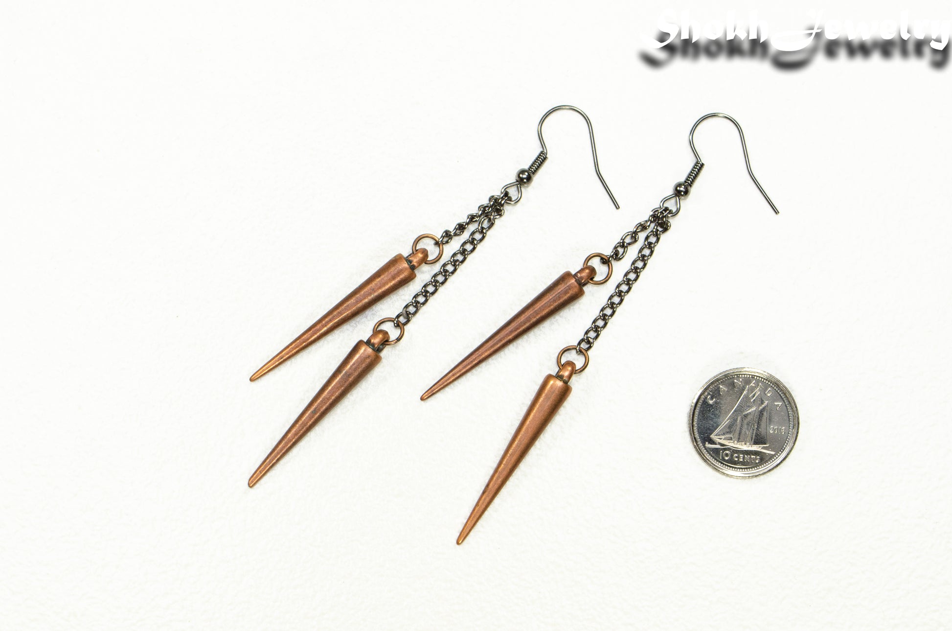 Long chain and antique copper spike earrings beside a dime.