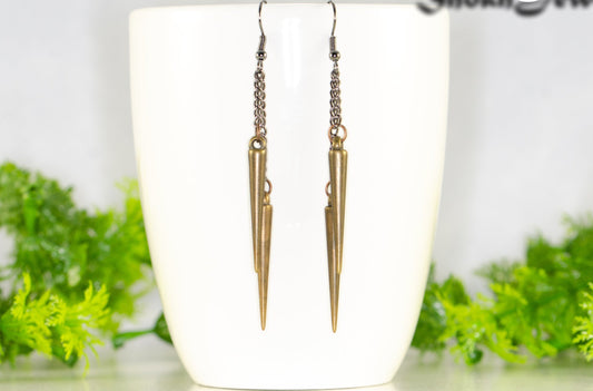 Long chain and antique bronze spike earrings displayed on a coffee mug.