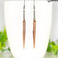 Long chain and antique copper spike earrings displayed on a coffee mug.
