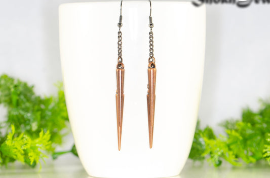 Long chain and antique copper spike earrings displayed on a coffee mug.
