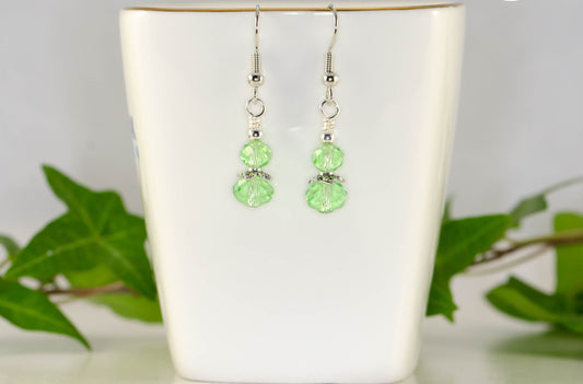 Small Light Green Glass Bead Dangle Earrings displayed on a tea cup.