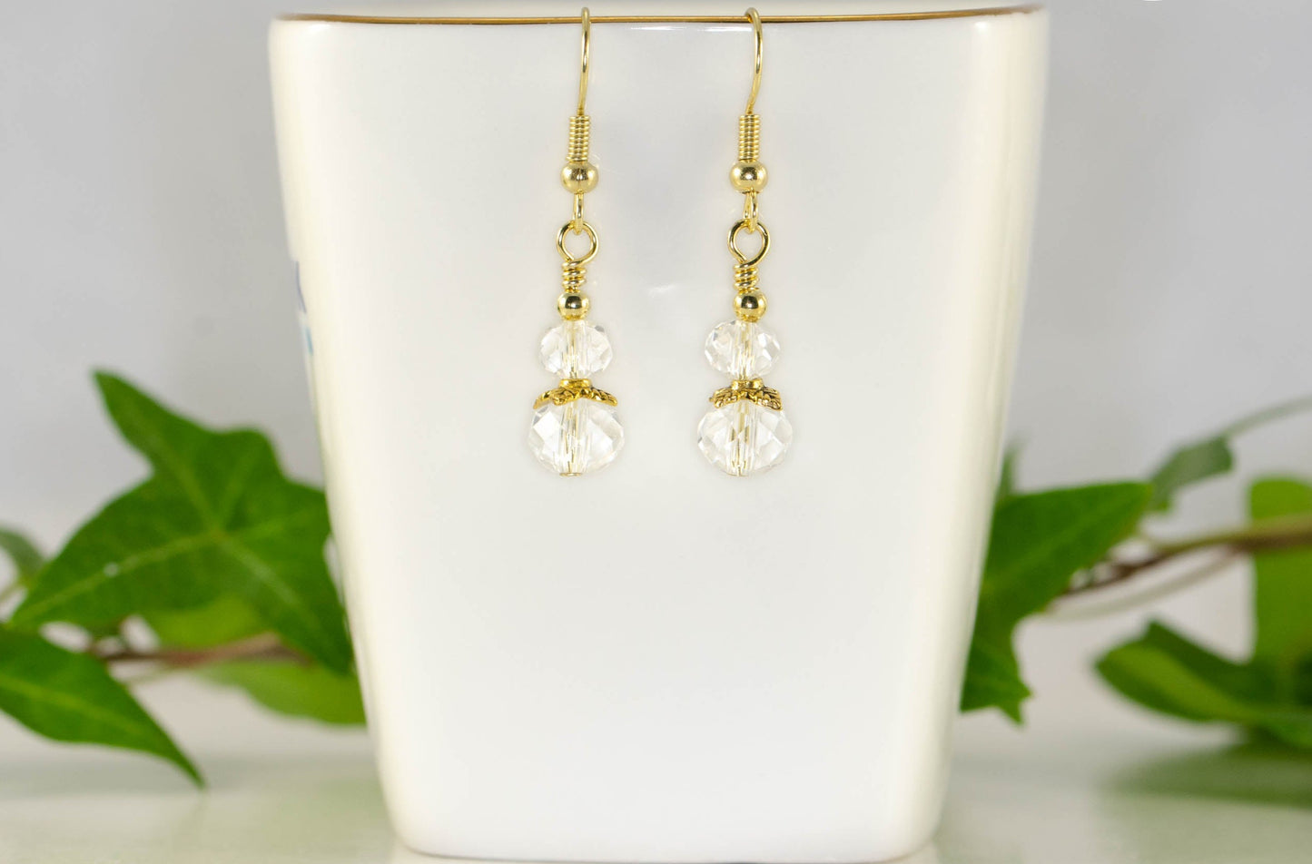 Small Clear Glass Bead Dangle Earrings displayed on a tea cup.