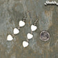 Long White Seashell Hearts Earrings beside a dime.