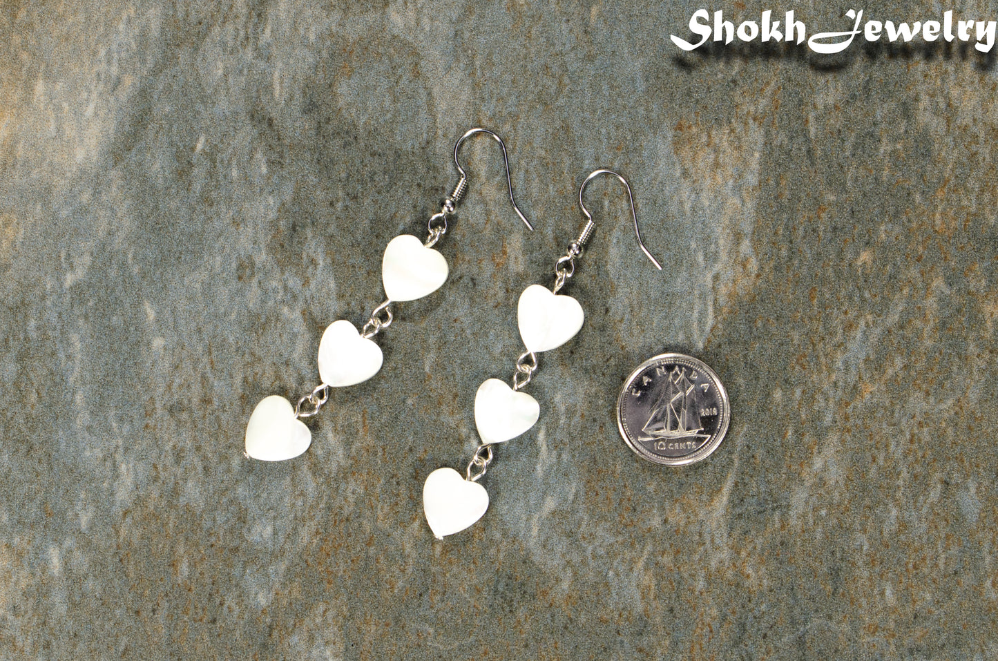 Long White Seashell Hearts Earrings beside a dime.