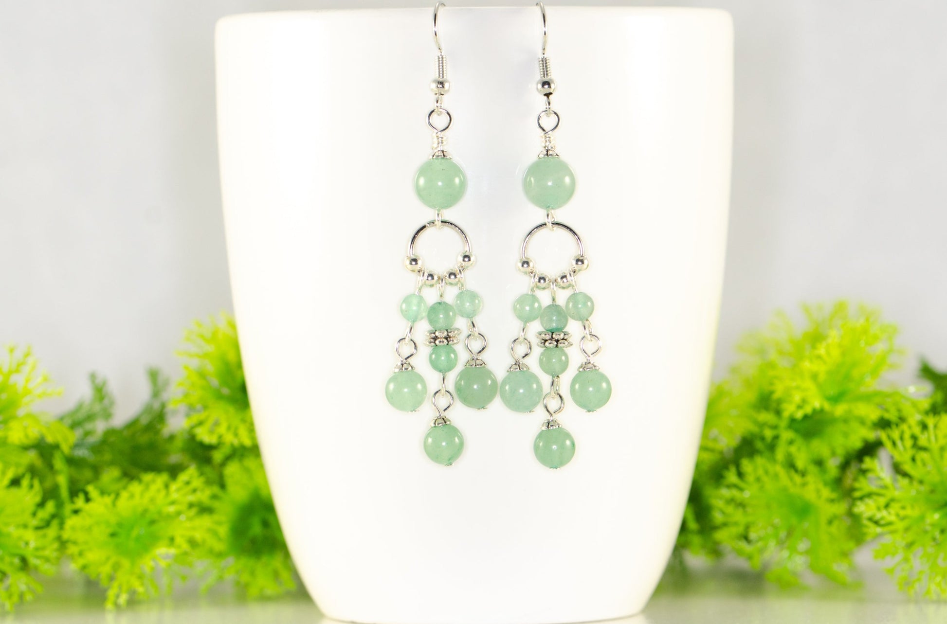 Statement Green Aventurine Crystal Chandelier Earrings displayed on a coffee mug.