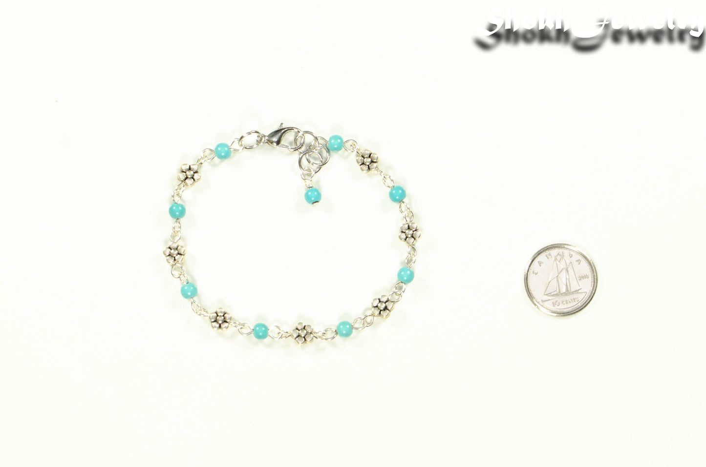 Tibetan Silver Flower and Turquoise Howlite Link Bracelet beside a dime.
