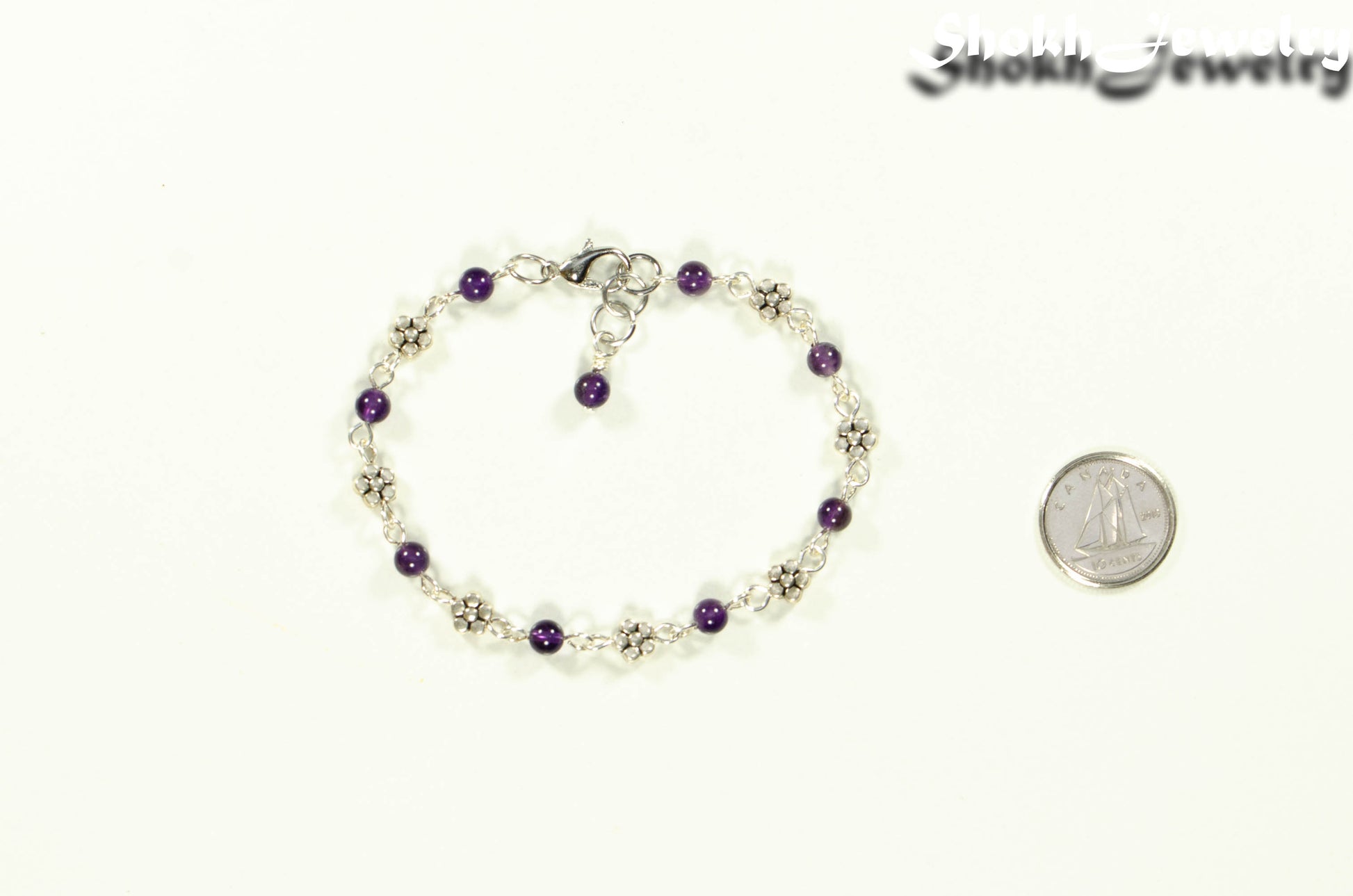 Tibetan Silver Flower and Amethyst Link Bracelet beside a dime.