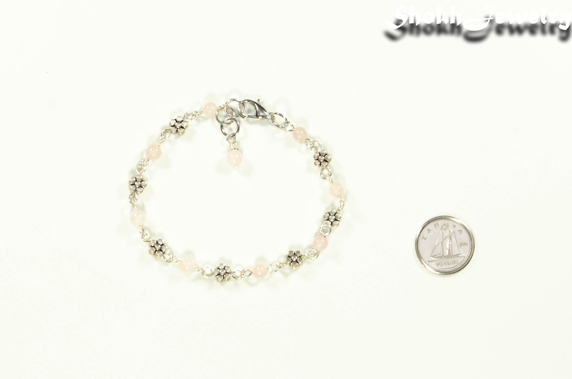 Tibetan Silver Flower and Rose Quartz Link Bracelet beside a dime.