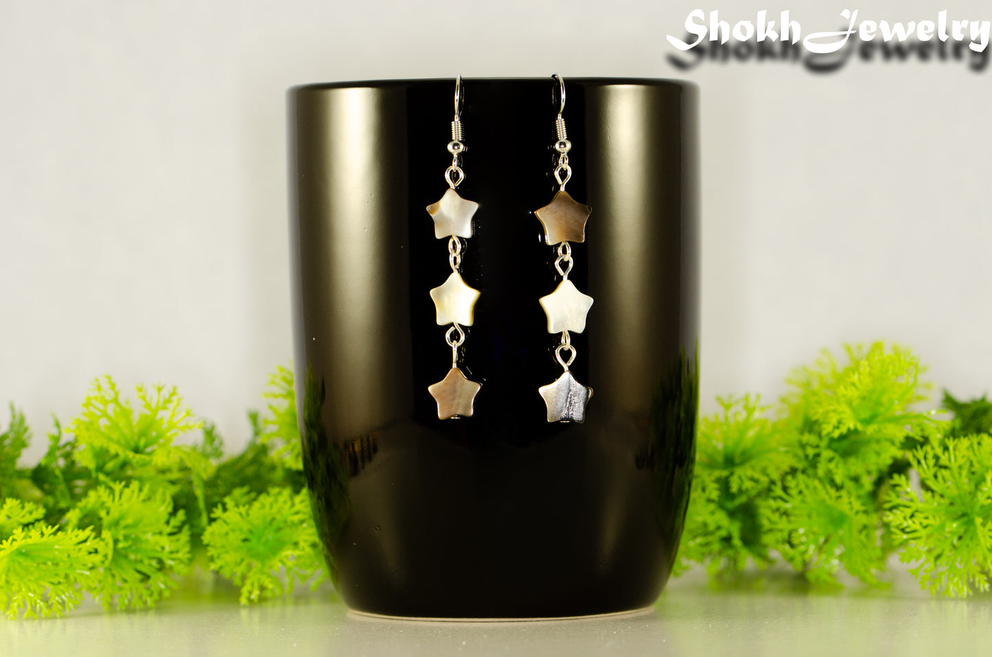 Long Natural Seashell Star Earrings displayed on a coffee mug.