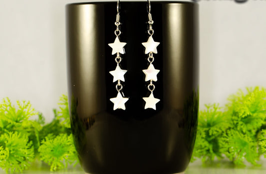 Long Natural White Seashell Star Earrings displayed on a coffee mug.