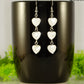 Long White Seashell Hearts Earrings displayed on a coffee mug.