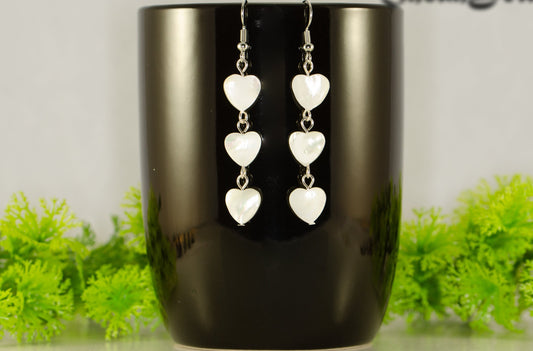 Long White Seashell Hearts Earrings displayed on a coffee mug.