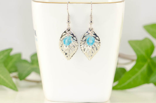 Filigree Leaf Charm and Aqua Blue Glass Crystal Earrings displayed on a tea cup.