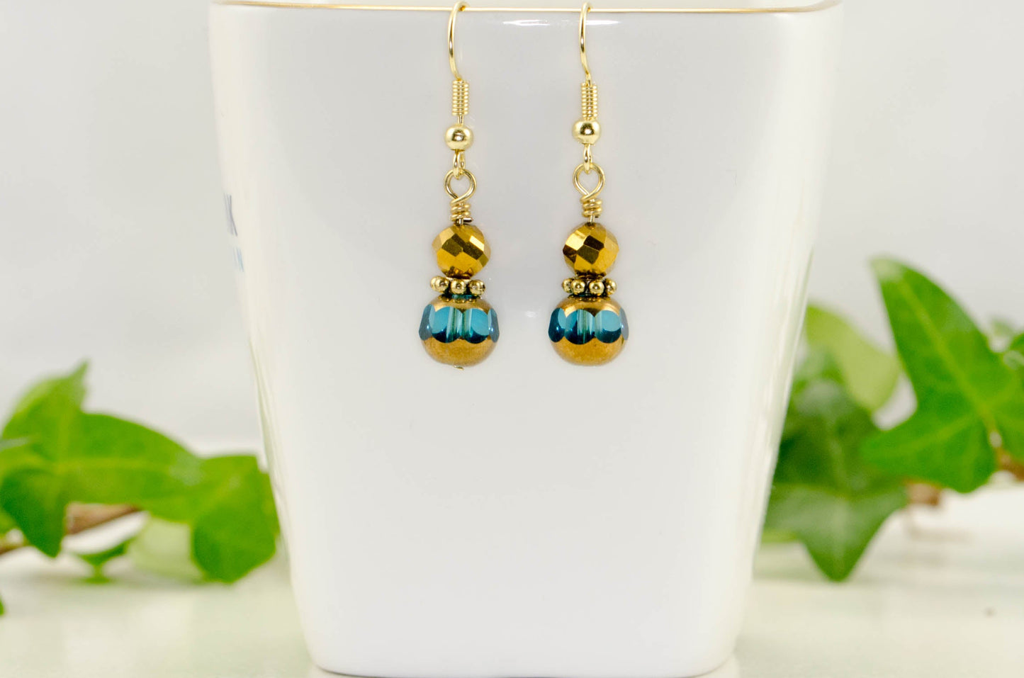 Small Patina Blue and gold Glass Bead Dangle Earrings displayed on a tea cup.