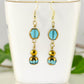 Sparkly Gold and Patina Blue Glass Bead Earrings displayed on a tea cup.