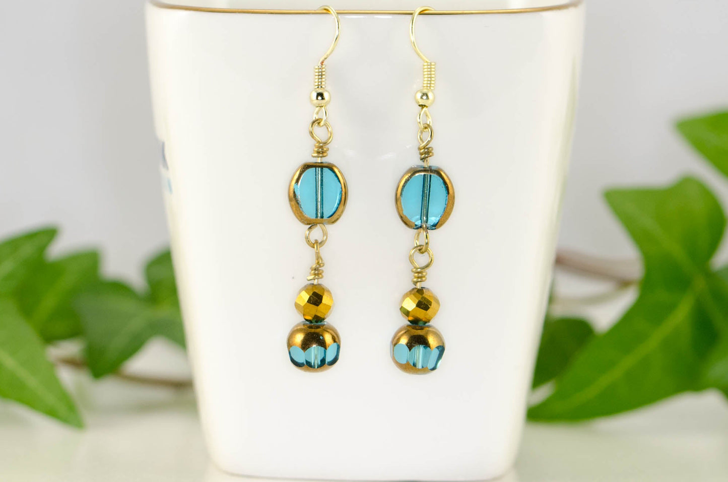 Sparkly Gold and Patina Blue Glass Bead Earrings displayed on a tea cup.