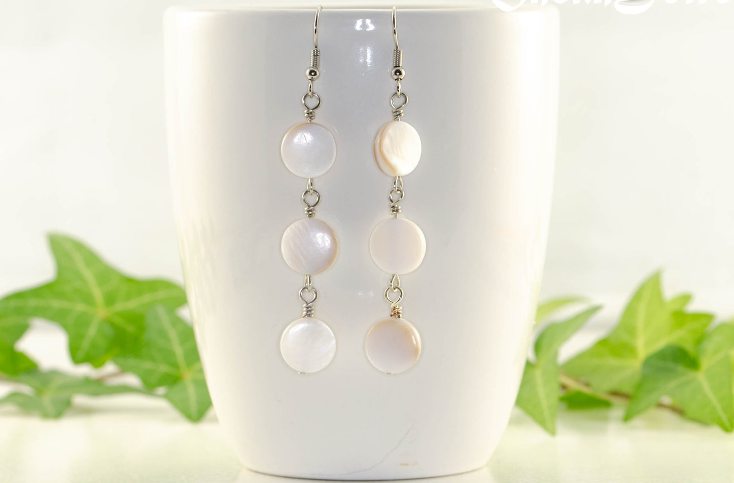 Long White Natural Seashell Earrings displayed on a coffee mug.