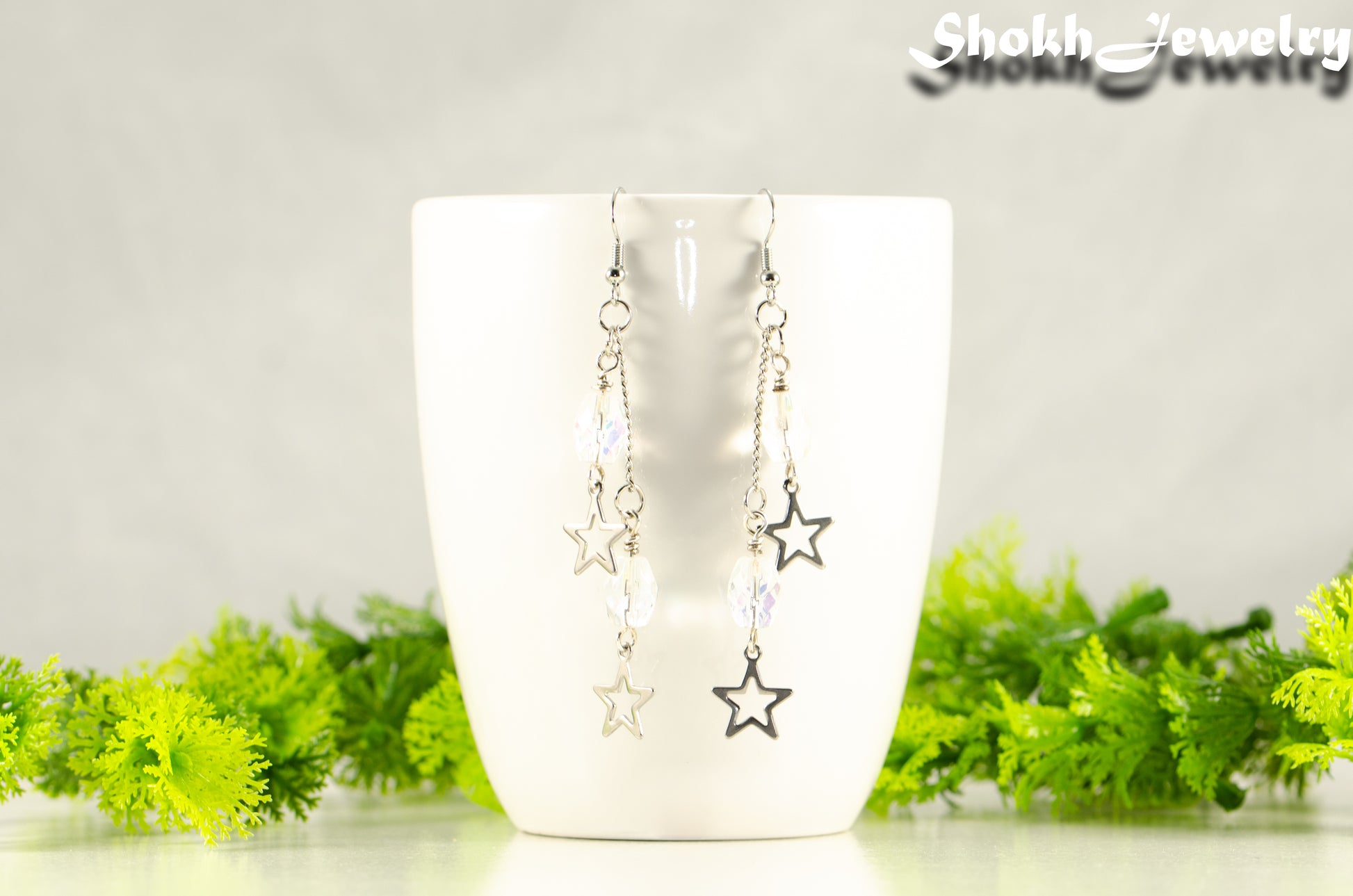 Clear Glass and Stainless Steel Star Earrings displayed on a white coffee mug.