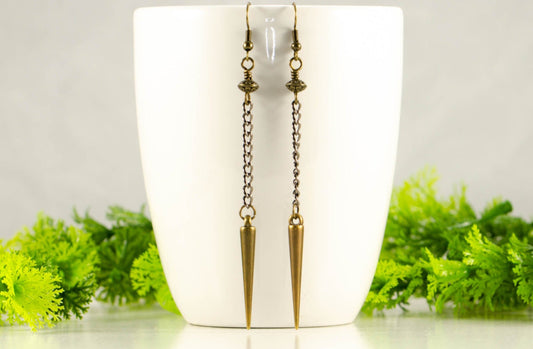 Statement chain and antique bronze spike earrings on a coffee mug