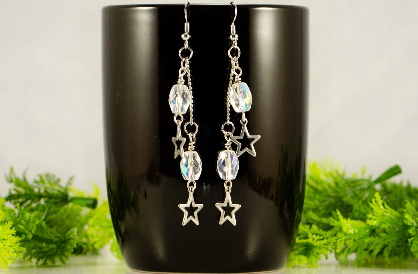 Clear Glass and Stainless Steel Star Earrings displayed on a black coffee mug.