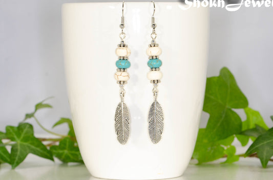 Statement White And Turquoise Howlite And Feather Earrings displayed on a coffee mug.