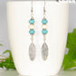 Statement Turquoise And White Howlite And Feather Earrings displayed on a coffee mug.