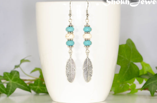 Statement Turquoise And White Howlite And Feather Earrings displayed on a coffee mug.