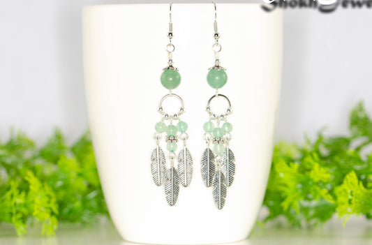 Statement Green Aventurine Crystal And Feather Earrings displayed on a coffee mug.