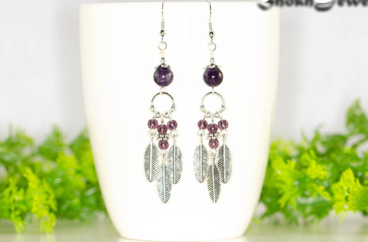 Statement Amethyst Crystal And Feather Earrings displayed on a coffee mug.
