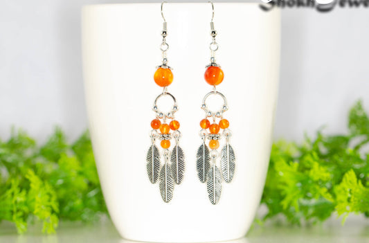 Statement Carnelian Crystal And Feather Earrings displayed on a coffee mug.