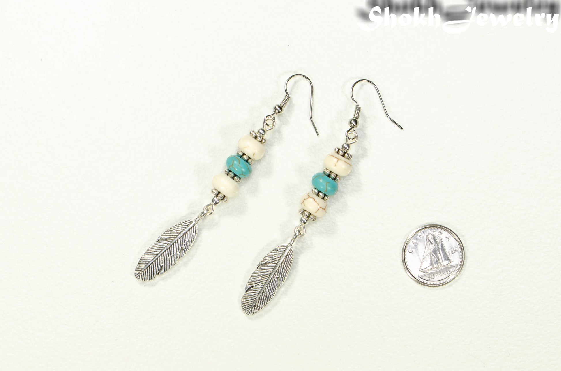 Statement White And Turquoise Howlite And Feather Earrings beside a dime.