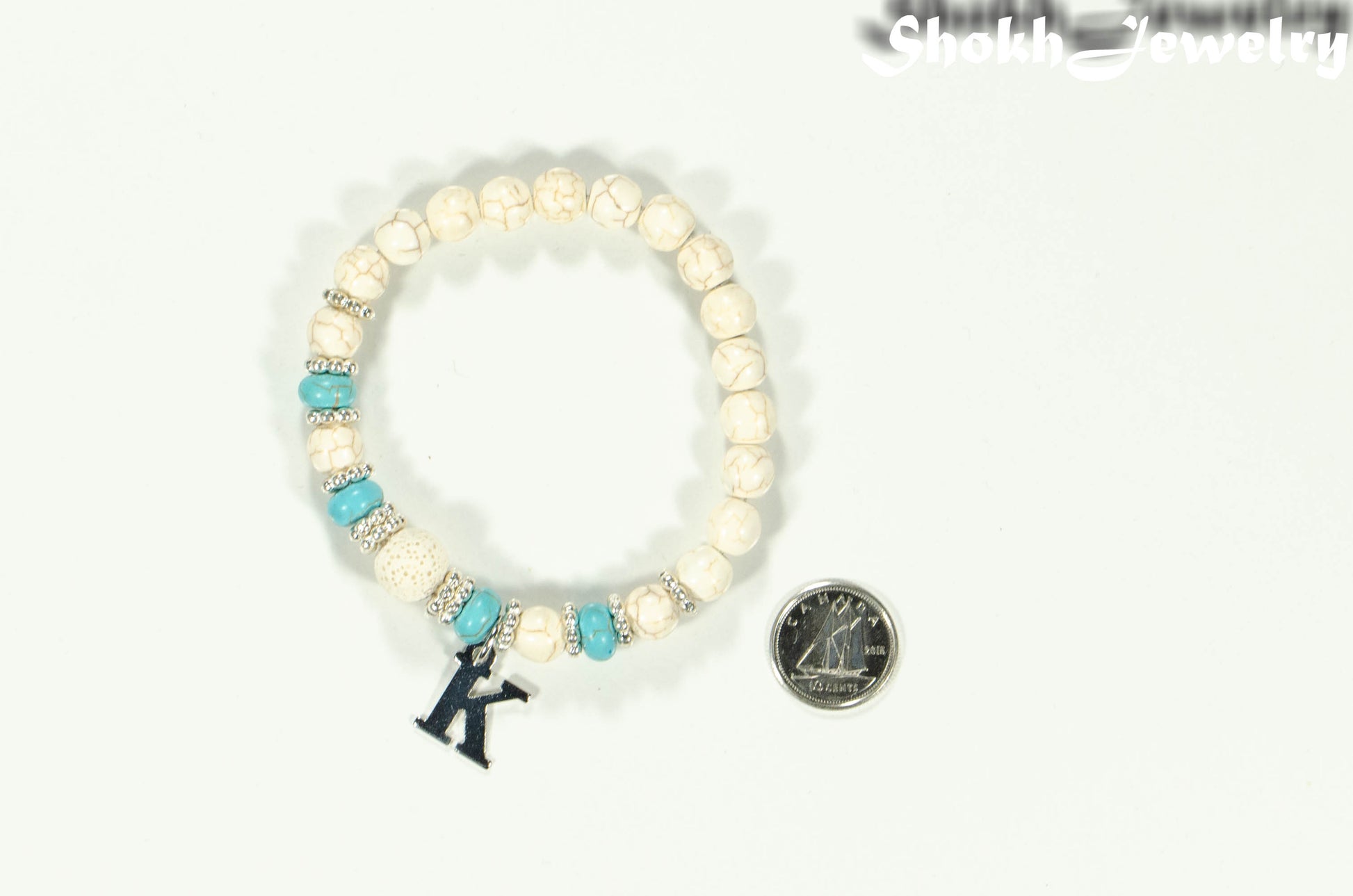 White Howlite and Lava Stone Bracelet with Initial beside a dime.